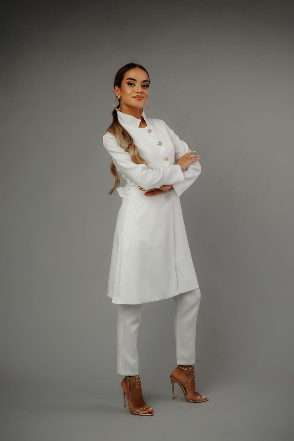 piękna_modelka_w_eleganckim_białym_żakiecie_i_spodniach_MedElite_na_szarym_tle_złote_sandały_dodają_elegancji.