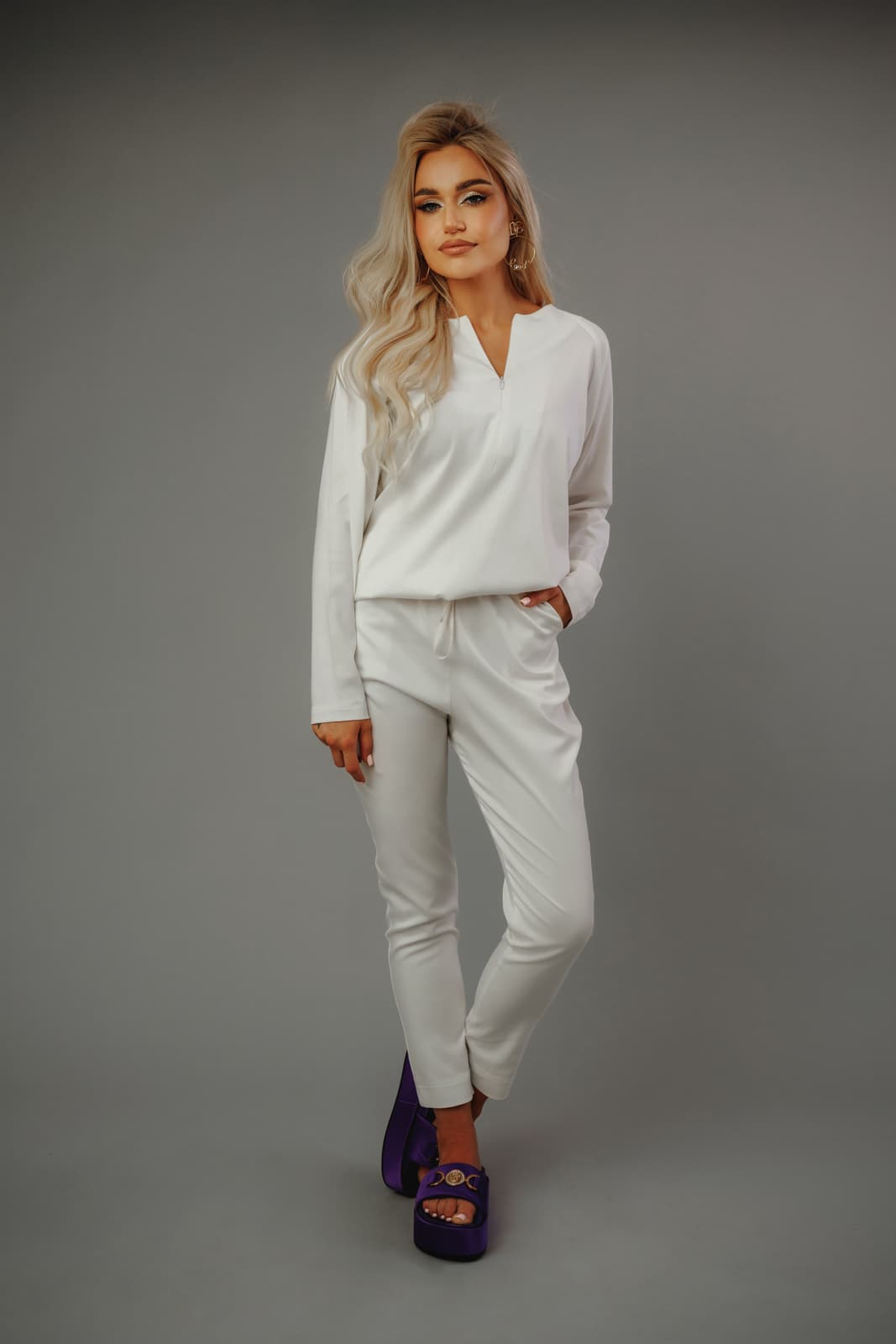 Modelka_w_białej_bluzie_i_spodniach_MedElite_na_szarym_tle_fioletowe_designerskie_obuwie_zrelaksowana