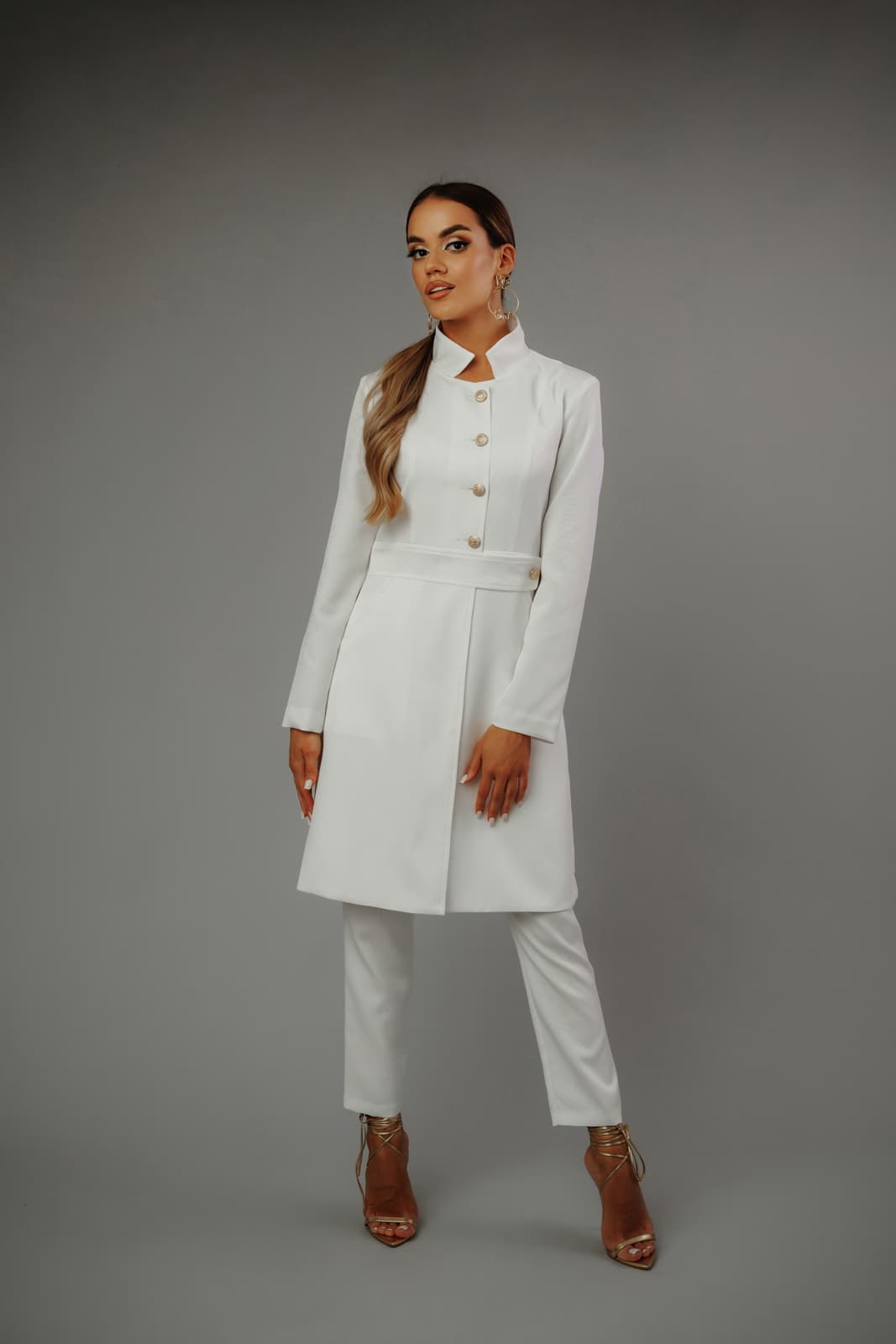 Modelka_w_eleganckim_białym_żakiecie_i_spodniach_MedElite_na_szarym_tle_złote_sandały_dodają_elegancji.